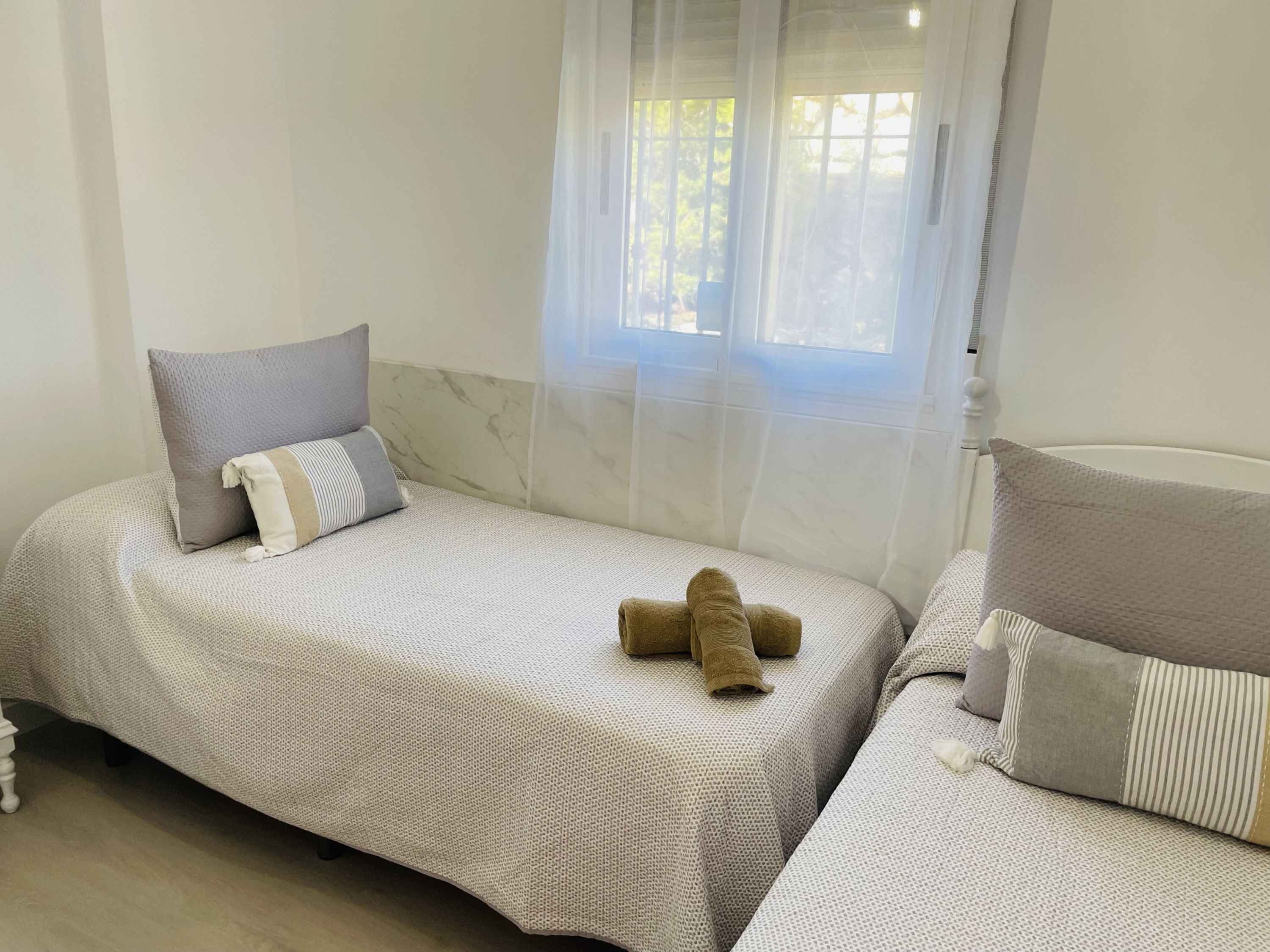 A bedroom with two beds, a window with sheer curtains, and a marble wall.