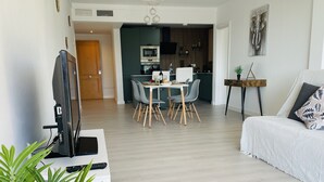 Una sala de estar moderna con televisor de pantalla plana, un comedor con mesa y sillas, una cocina equipada y una cama con almohada.