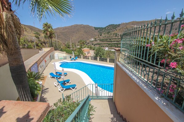 A swimming pool with blue water, surrounded by a green fence and palm trees. - Apartamento Altos de Tamango con Vistas y Pisicina (Torrox)