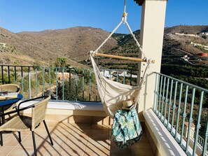 A balcony with a hammock, wicker furniture, and a view of a hilly landscape. - Apartamento Altos de Tamango con Vistas y Pisicina (Torrox)
