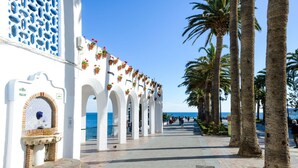 A seaside promenade with white buildings, palm trees, and a clear blue sky. - Apartamento Cantarero by At Home Costa del sol (Nerja)