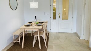Zona pranzo con tavolo di legno apparecchiato per quattro persone, lampada a sospensione e porta bianca con finestra.