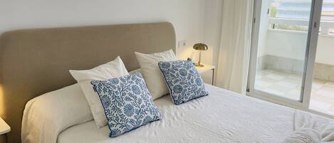 Habitación de hotel con cama, dos almohadas, mesita de noche, lámpara y vistas al exterior.