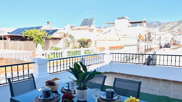 A table with a view of a cityscape, a potted plant, and a fruit basket.