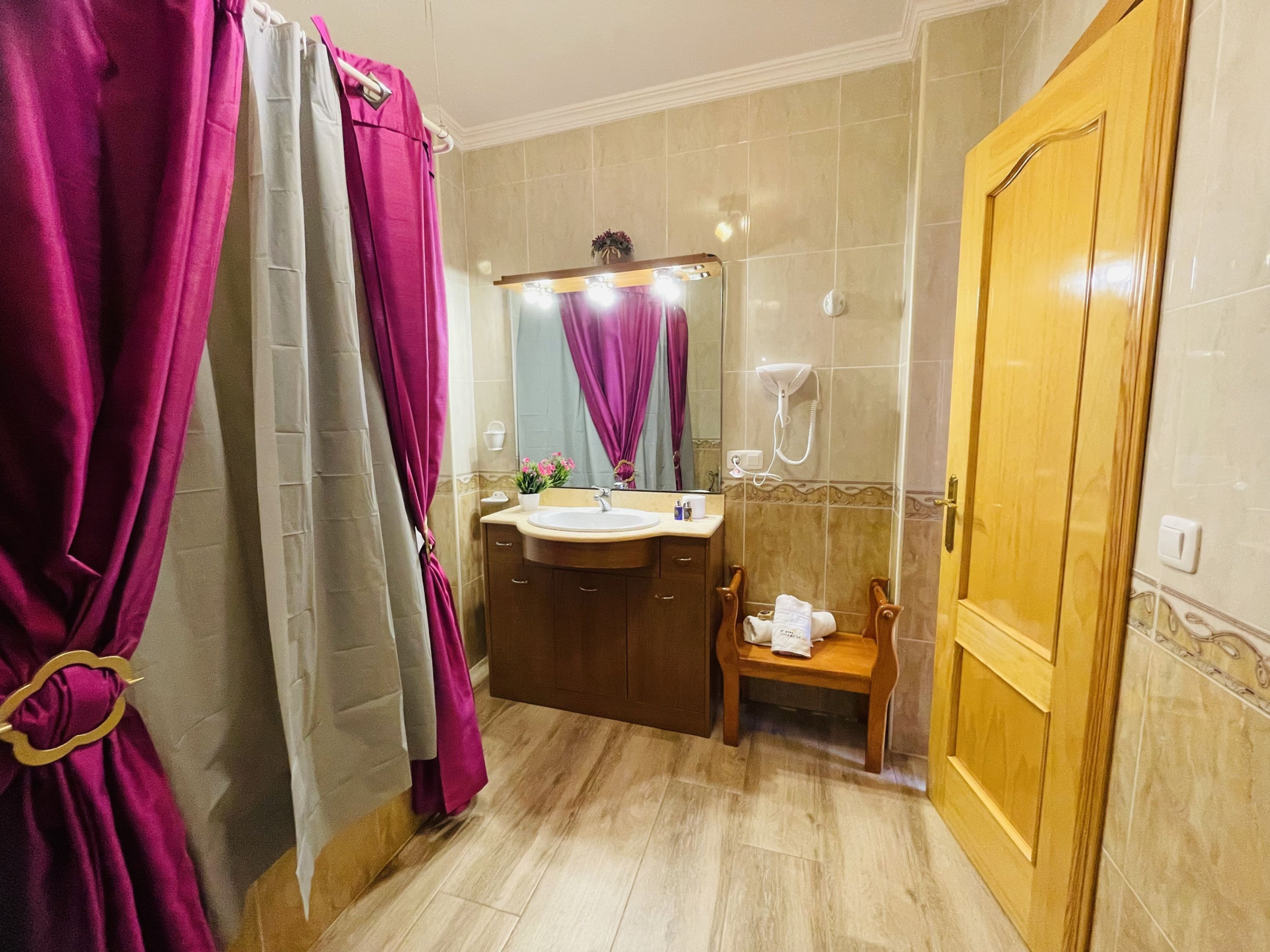 Une salle de bain avec un lavabo, un miroir, un rideau de douche et une porte en bois.