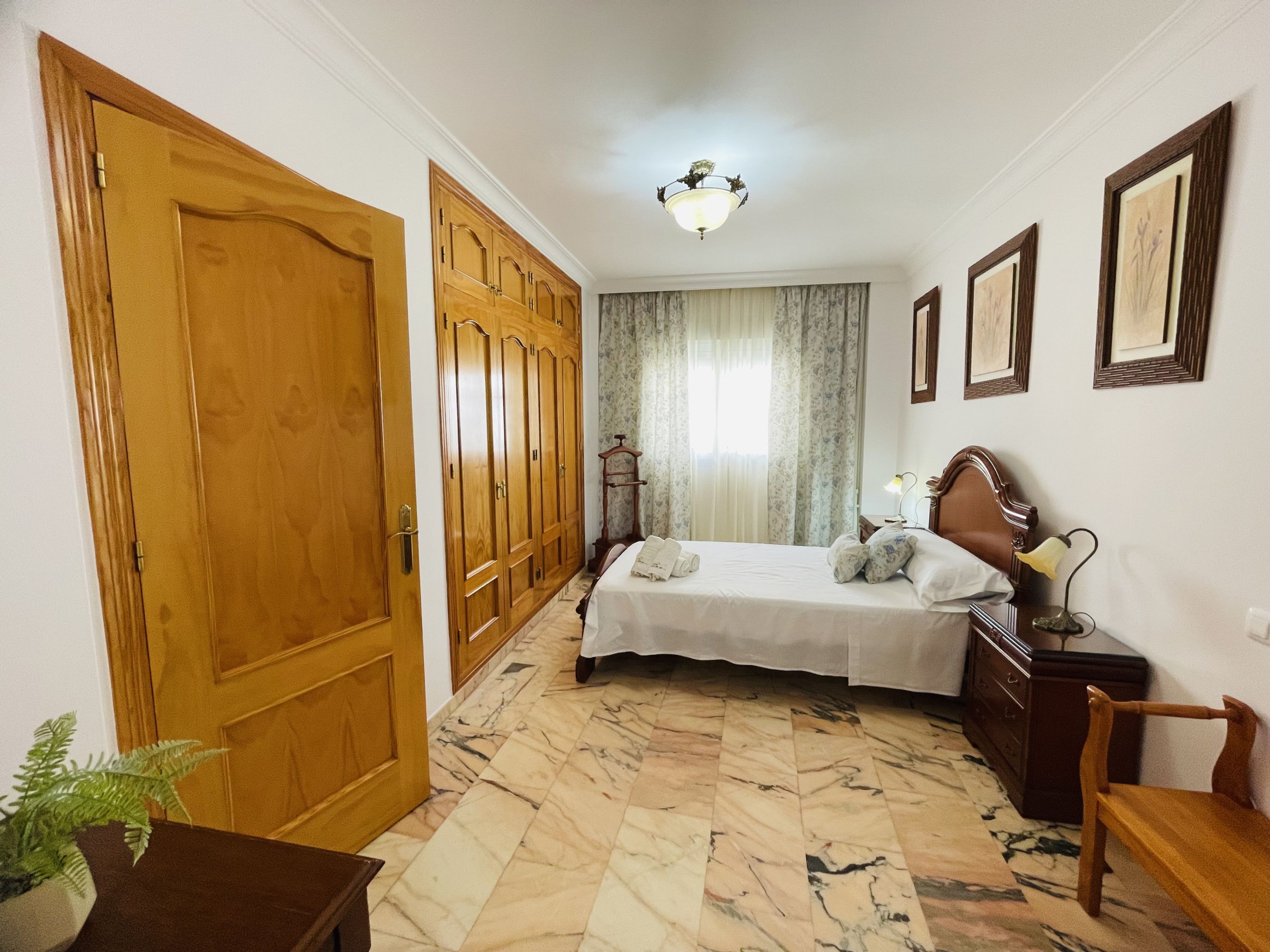 Un dormitorio con cama, armario de madera, suelo de mármol y una lámpara de techo.