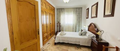 Un dormitorio con cama, armario de madera, suelo de mármol y una lámpara de techo.