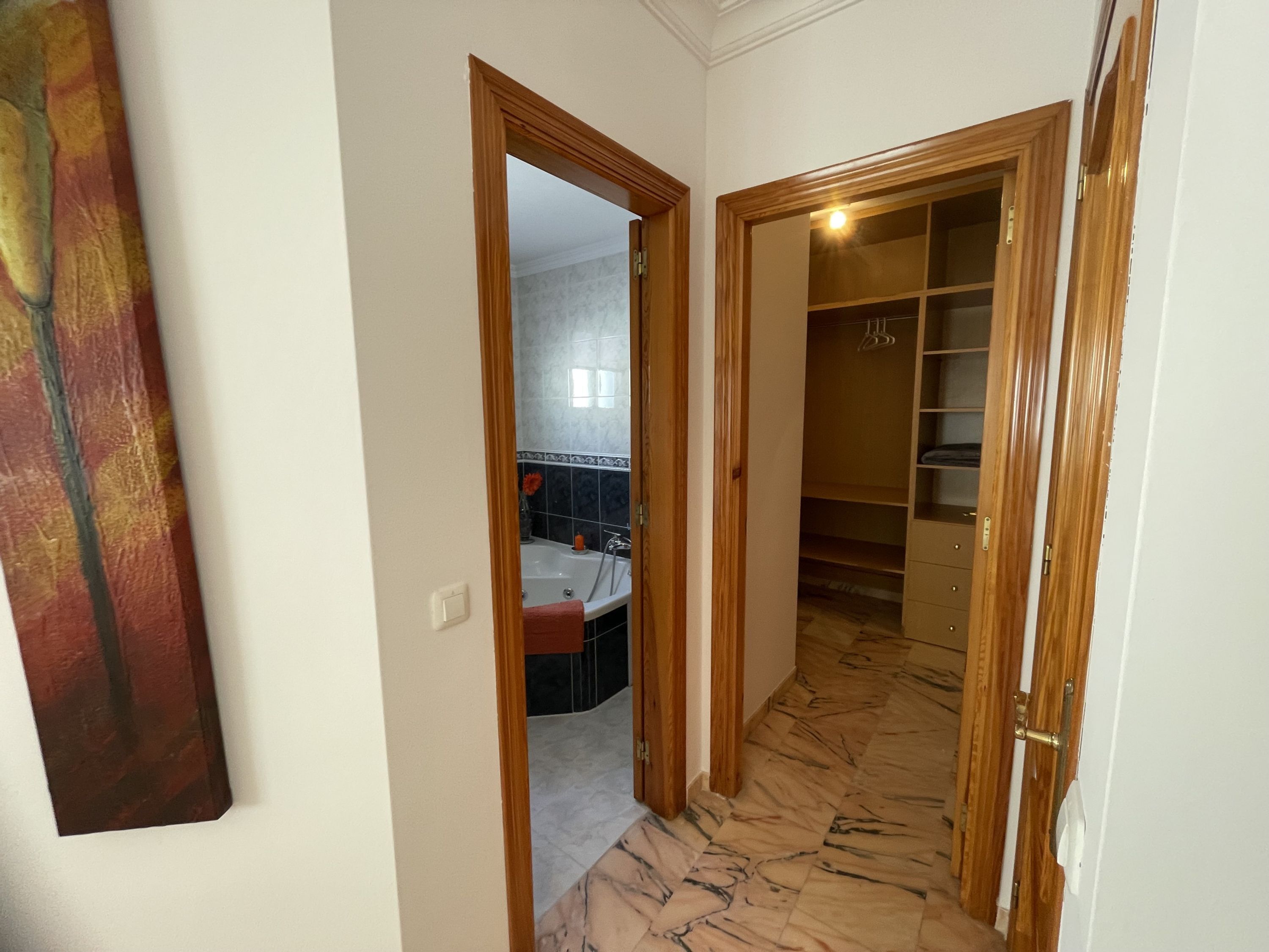 A hallway with a mirror, a wooden door, and a tiled floor.