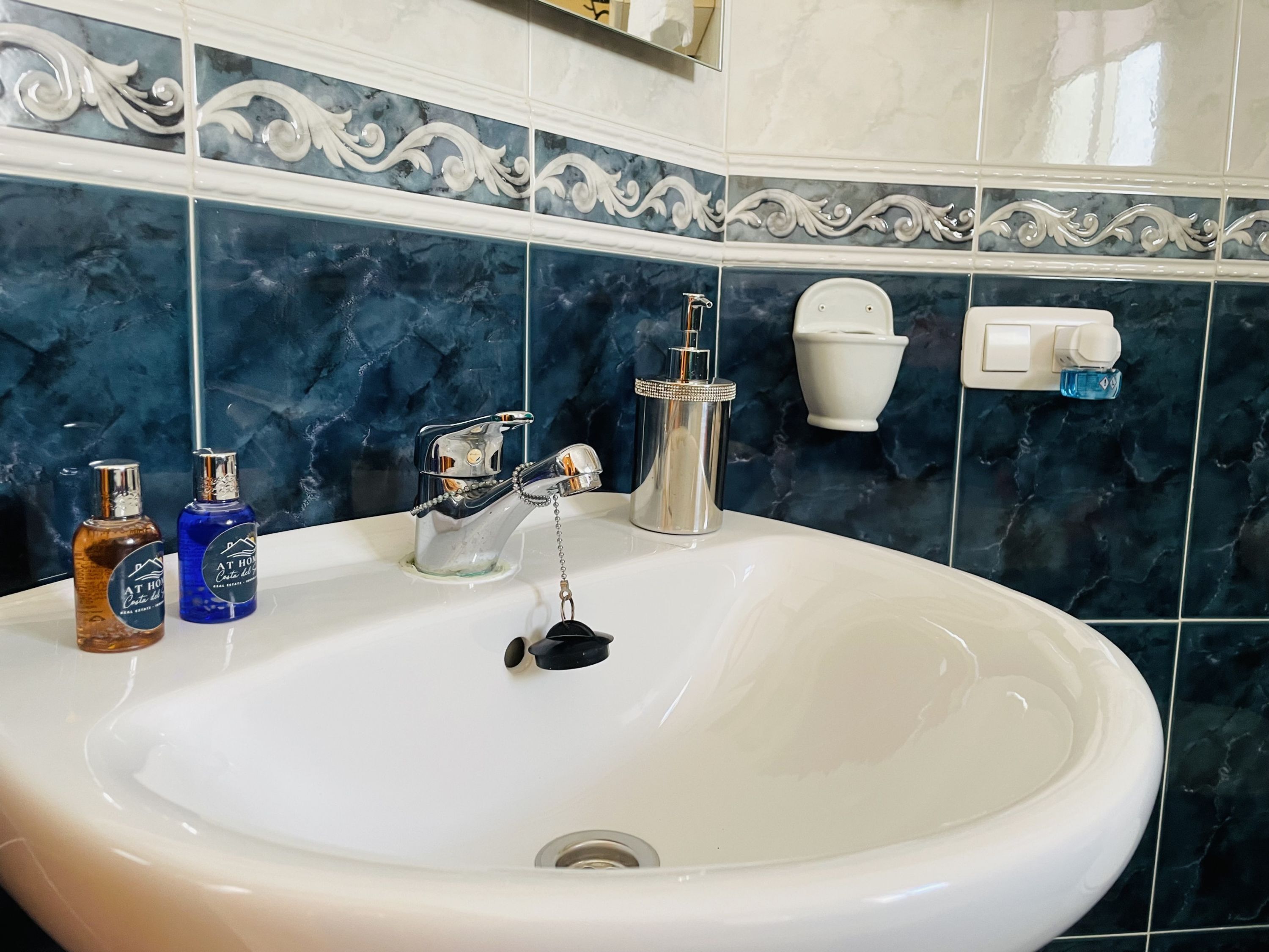 A bathroom with a white sink, two bottles of hand soap, a faucet, and a toilet paper holder.