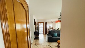 A hallway leading to a living area with a sofa, a dining table, and a chandelier.