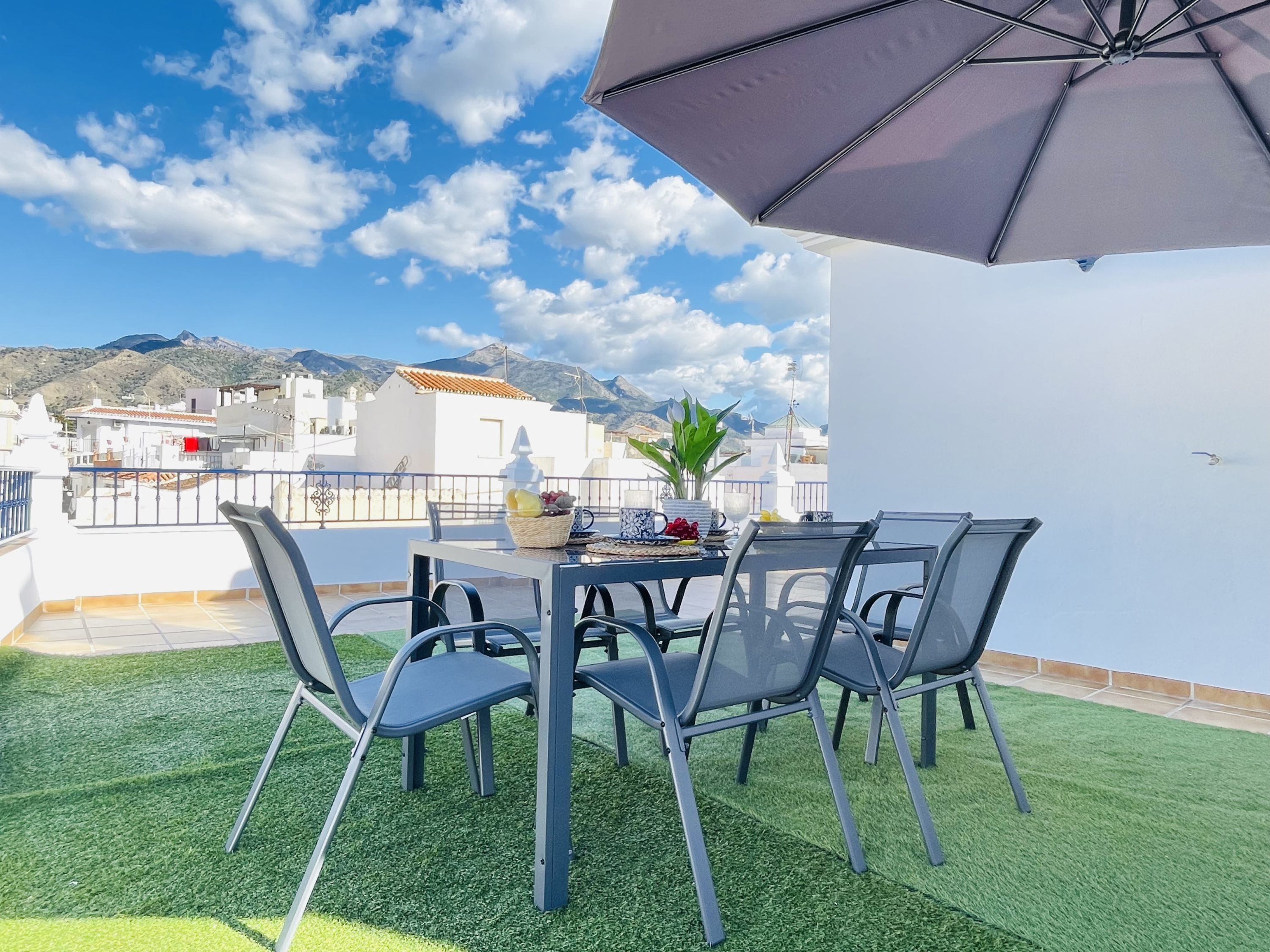 A terrace with a table and chairs, a potted plant, and a large umbrella.