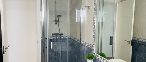 A modern bathroom with a glass-enclosed shower, a white sink with a decorative tile border, and a potted plant.