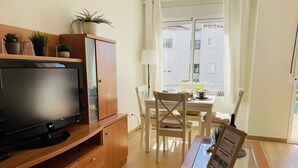 Una sala de estar moderna con un televisor de pantalla plana, muebles de madera, una mesa de centro de vidrio y vistas al exterior a través de una ventana con cortinas.
