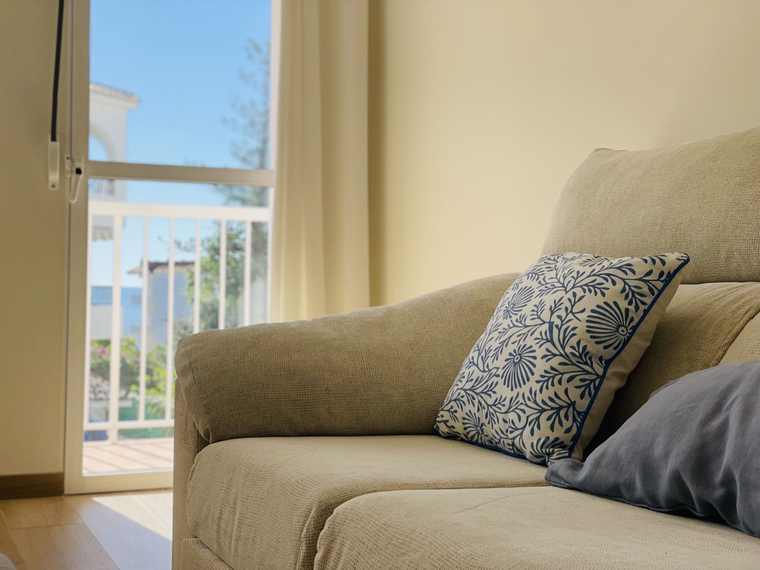 A beige sofa with a patterned pillow and a plain pillow, positioned near a sliding glass door leading to an outdoor area.