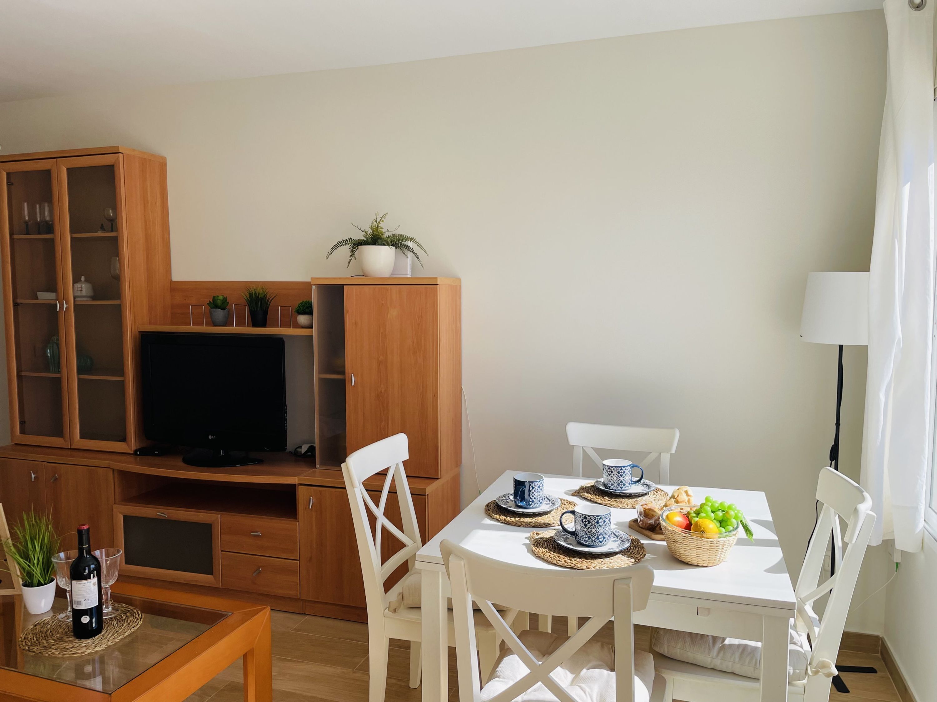 Ein modernes Wohnzimmer mit Fernseher, Holzschrank, Esstisch mit Stühlen und einer kleinen Küchenzeile.
