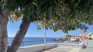 Un paseo marítimo con vistas claras al mar, un edificio blanco con barandilla azul y una bandera.