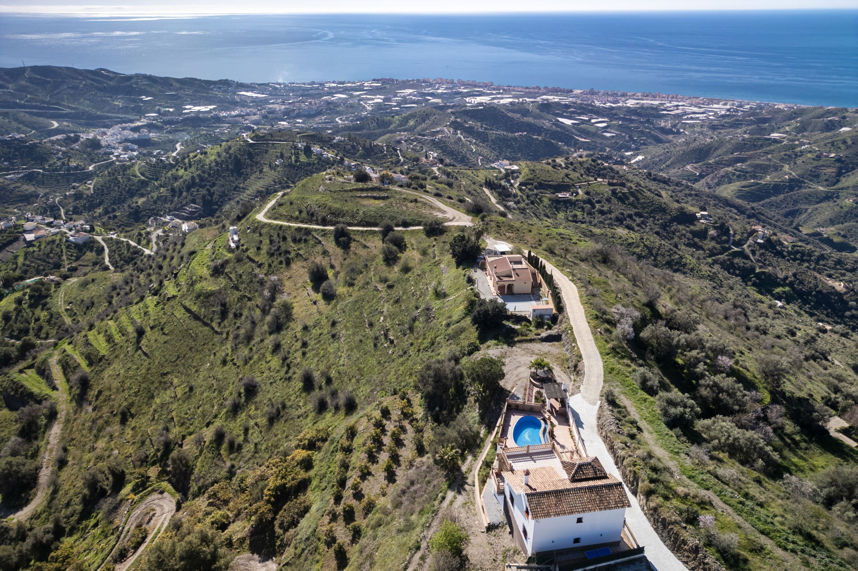 An aerial view of a property with terraced fields, a swimming pool, and a path leading to a building.