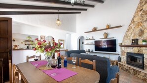 A dining area with a wooden table, chairs, and a vase of flowers. There is a television and a fireplace in the background. - Casa Baena by At Home Costa del sol (Torrox)