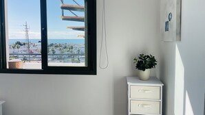 A room with a window overlooking a coastal cityscape, a white dresser with drawers, and a potted plant. - Apartamento Mar de Nerja Sunset (Nerja)