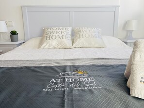 Una cama bien hecha con dos almohadas, una colcha gris y un logotipo en la colcha.