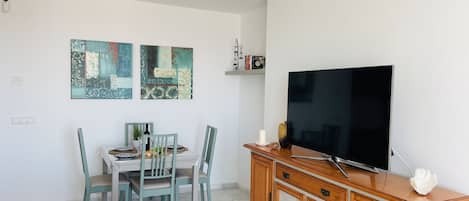 Un salon moderne doté d’un téléviseur à écran plat, d’un coin repas avec une table et des chaises, et d’un canapé gris.