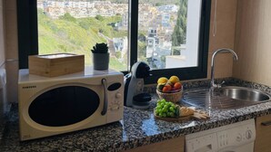 Een keuken met een magnetron, spoelbak en uitzicht op een heuvelstad.