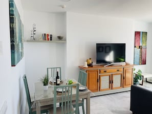 Een moderne woonkamer met een eettafel, stoelen, een televisie en een boekenkast.