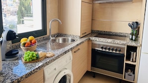 Een moderne keuken met een RVS-spoelbak, een granieten aanrechtblad, een inbouwoven en een wasmachine.