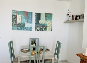 A dining area with a white table, two chairs, a wine bottle, and a plate of food. There are two abstract paintings on the wall above the table. - Apartamento Mar de Nerja Sunset (Nerja)