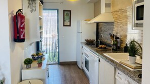 A modern kitchen with white cabinets, a built-in oven, a microwave, and a sink. There is a hanging plant, a fire extinguisher, and a window with curtains. - Cortijo Montesue os con Vistas by At Home Costa de (Torrox)
