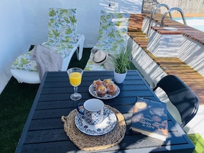 Pátio com mesa posta para o café da manhã, incluindo um copo de suco de laranja, doces, uma xícara de chá e um livro.