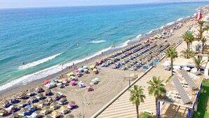 A beach with rows of sun loungers and umbrellas, a clear blue sea, and a few people in the water. - Casa Ascen by At Home Costa del Sol (Torrox)