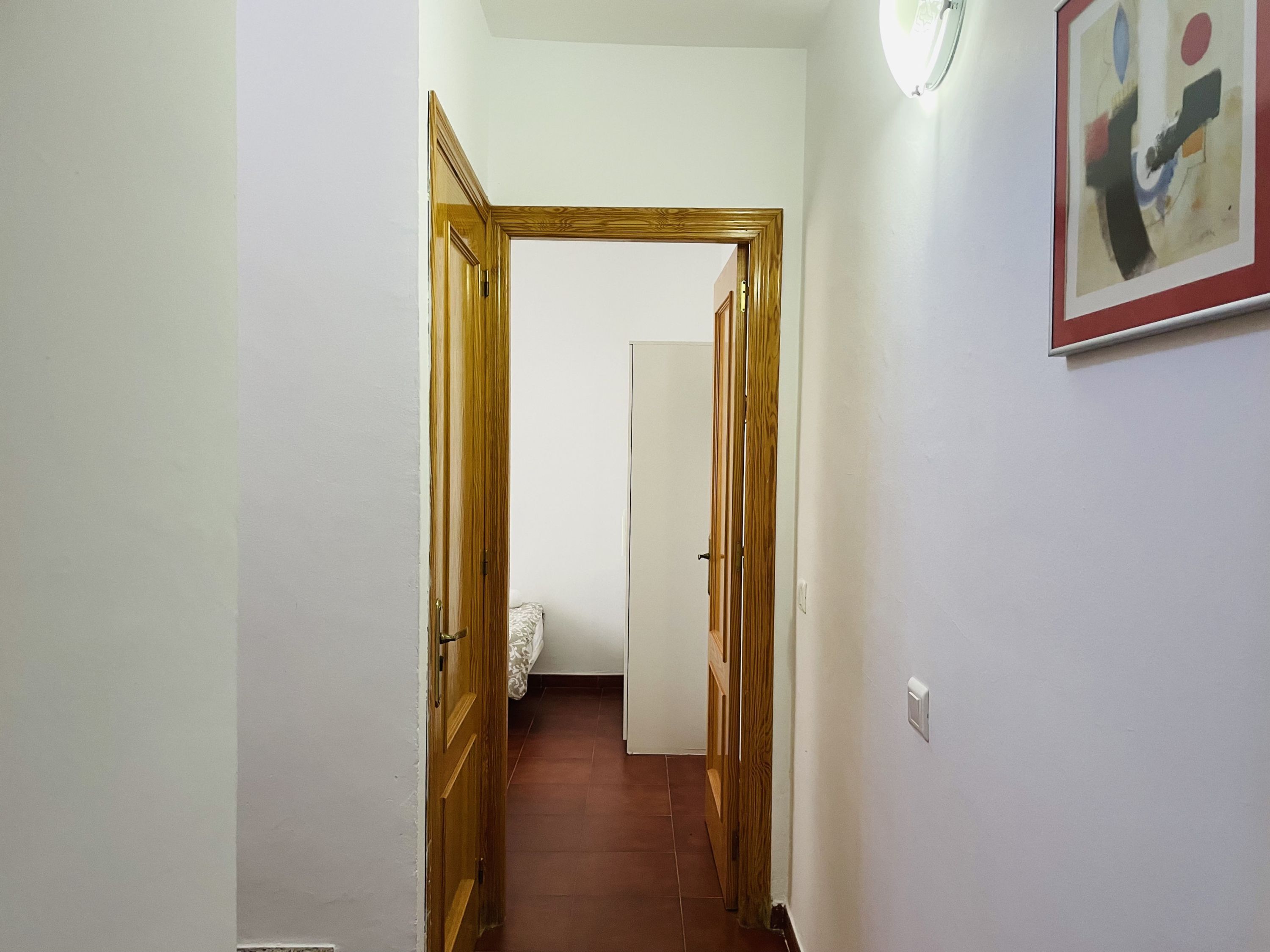 Un pasillo con puertas de madera y una pared blanca con un cuadro abstracto enmarcado.