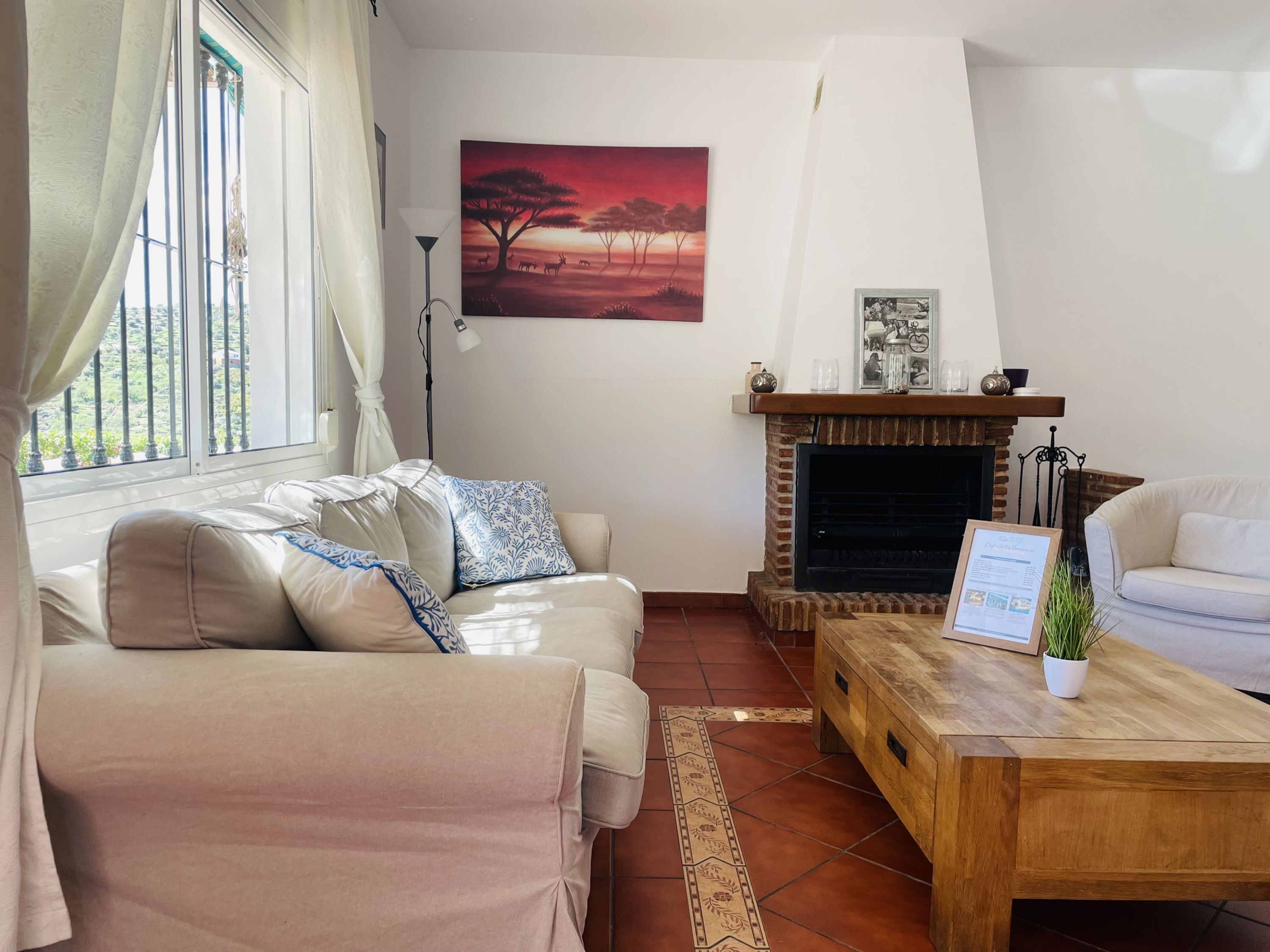 A living room with a beige sofa, a coffee table, a fireplace, and a painting of a sunset.