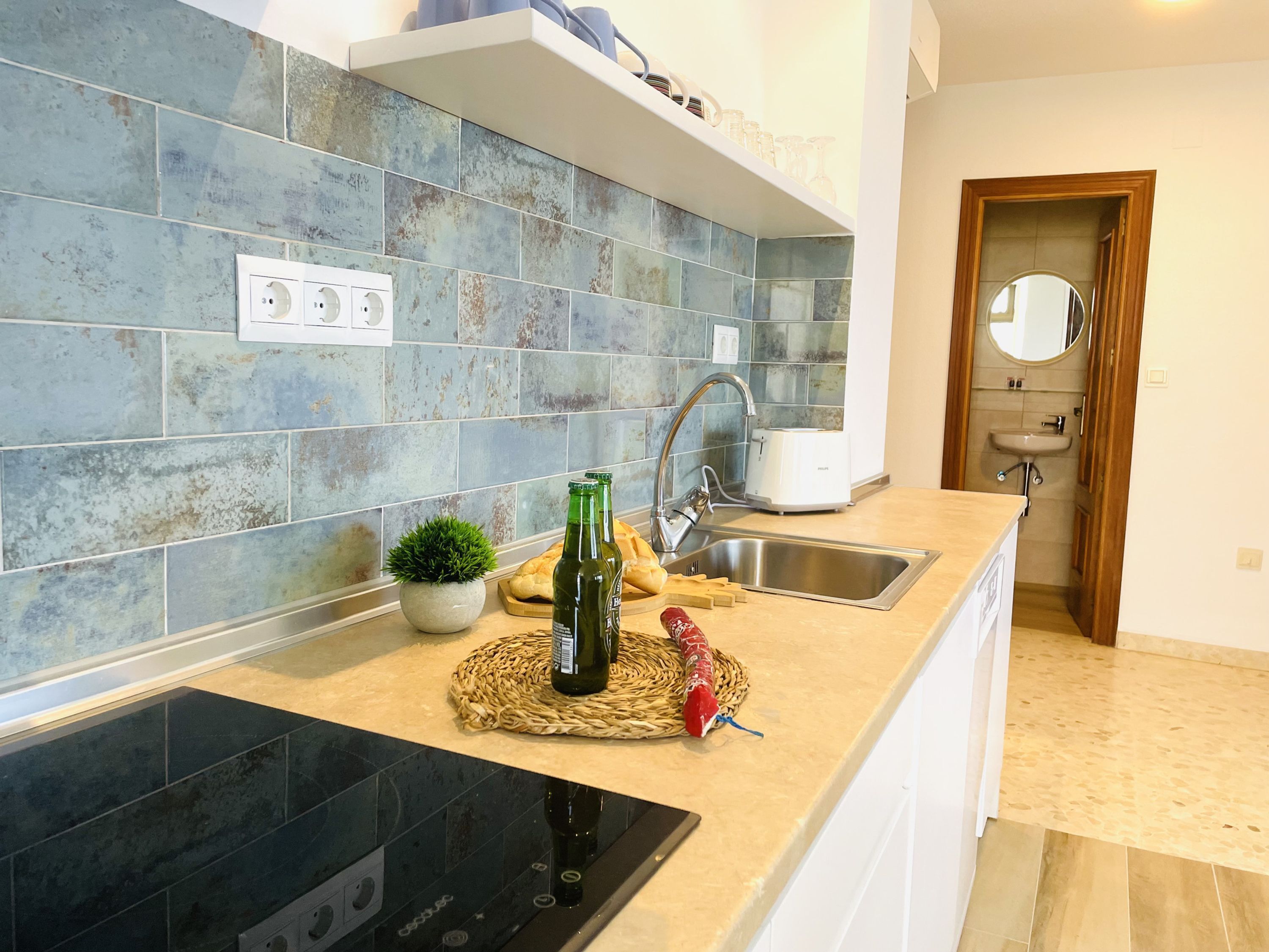 A kitchen with blue tiles, a built-in oven, a sink, and a toaster.
