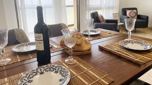 Une table à manger dressée avec des assiettes, des verres et une bouteille de vin, avec un canapé et une plante en arrière-plan.