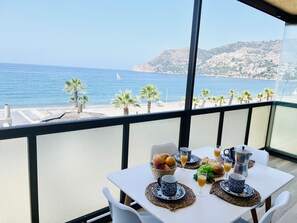 A balcony with a table set for breakfast overlooking a beach.