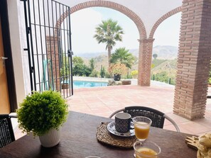 Une terrasse avec une table dressée pour deux personnes, une vue sur une piscine et un paysage montagneux.