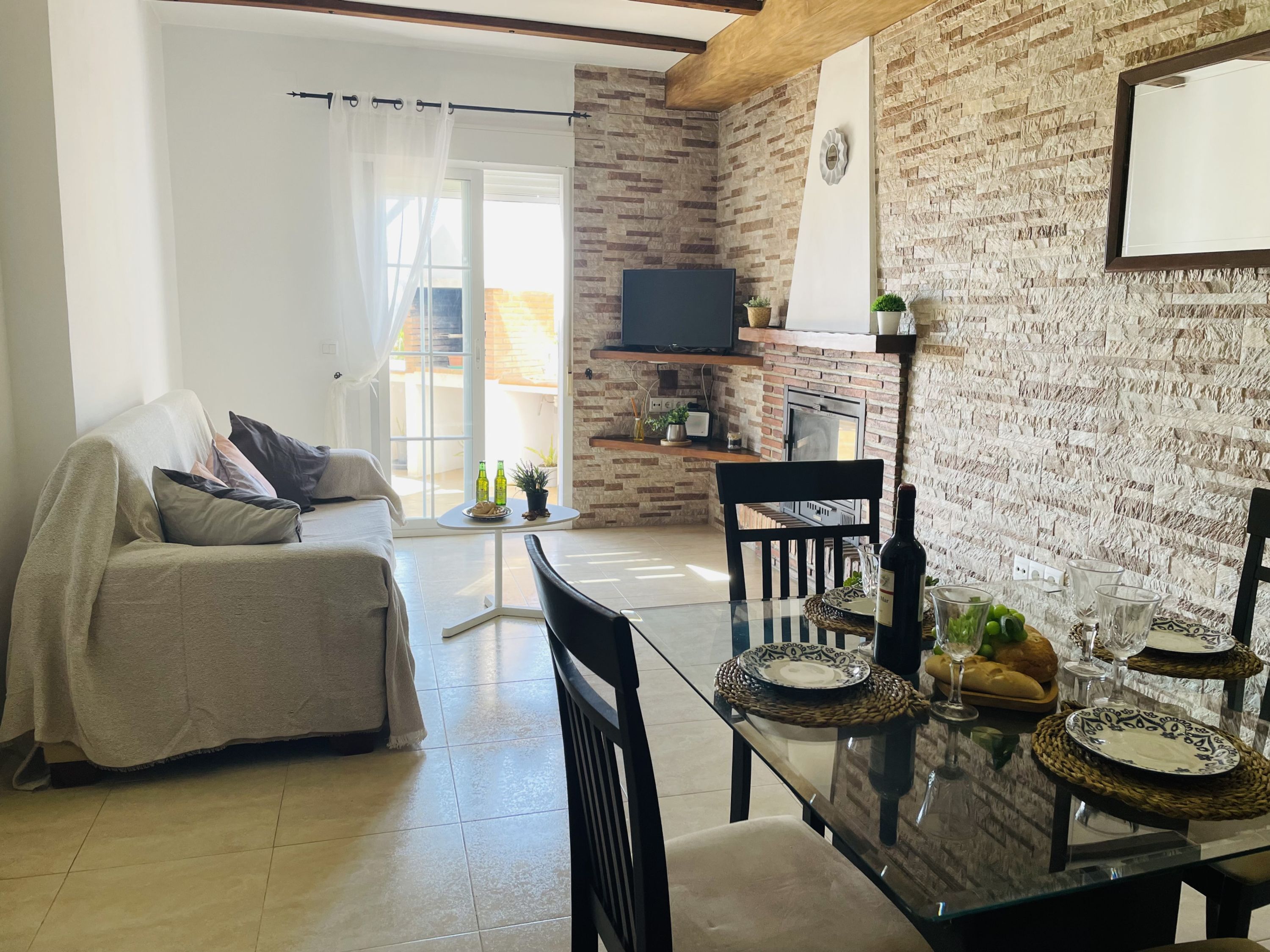 Una sala de estar con un sofá, una mesa de comedor servida con platos y vasos, un televisor y una pared de ladrillo.