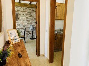 A wooden dining table with a framed menu, a fan, and a plant. A kitchen with wooden cabinets and a tiled backsplash is visible through an open doorway. - Casa Blanca con Vistas al mar by At Home Costa del (Torrox)