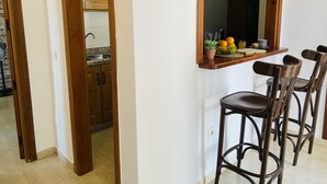 Una cocina con armarios de madera, un lavamanos y una cesta de fruta sobre una repisa. Hay tres taburetes de bar de madera y un espejo sobre la encimera.