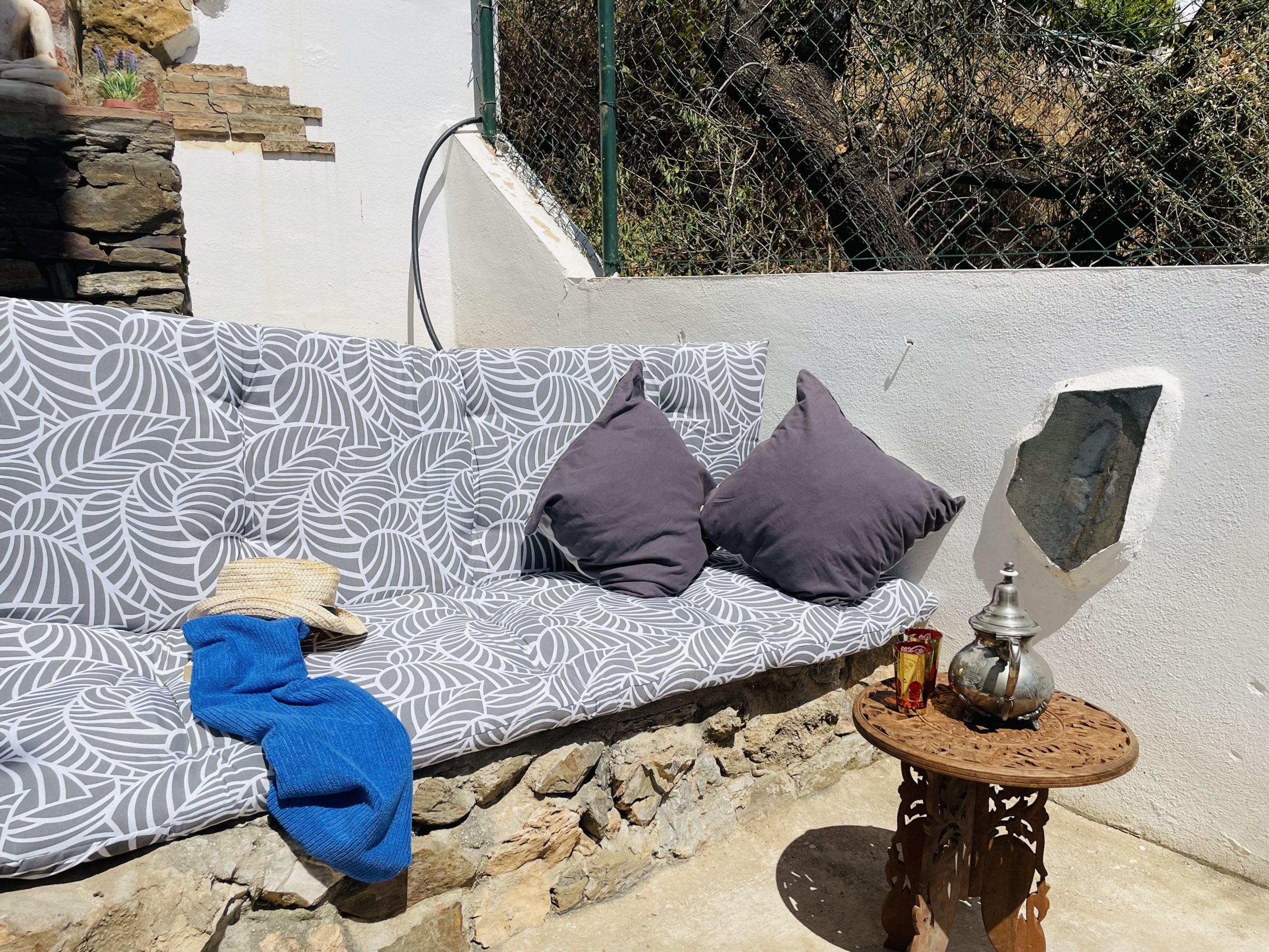 A stone wall, a patterned sofa, and a small wooden table with a metal pot.