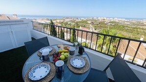 En balkon med et bord dækket til to personer, med tallerkener, kopper og en frugtkurv.