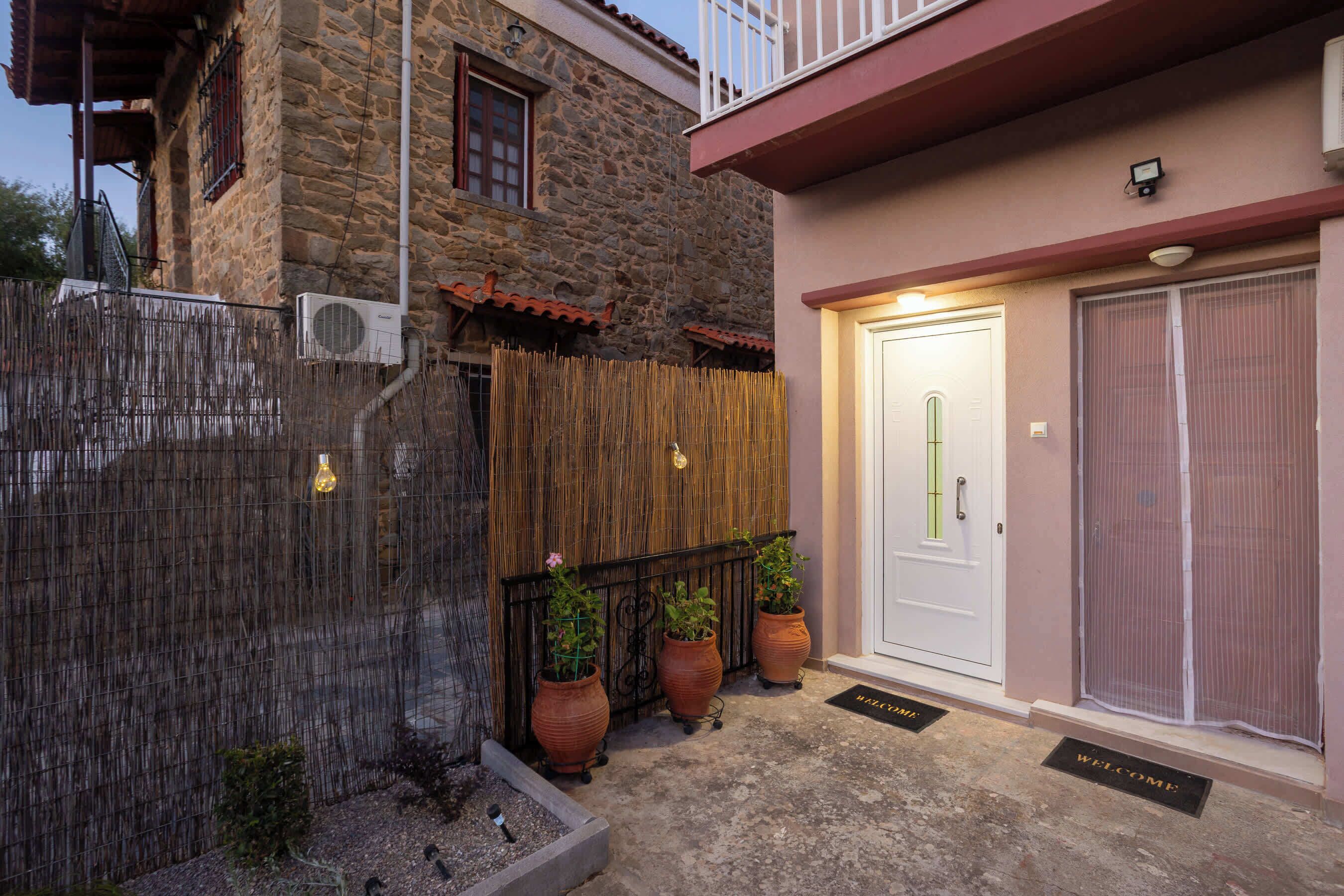 Un bâtiment en pierre avec une clôture en bois, une porte blanche et des plantes en pot.