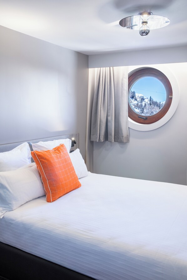 A bedroom with a bed, a round window with a view of a snowy landscape, and a ceiling light fixture. - PopAlp la Plagne (La Plagne-Tarentaise)