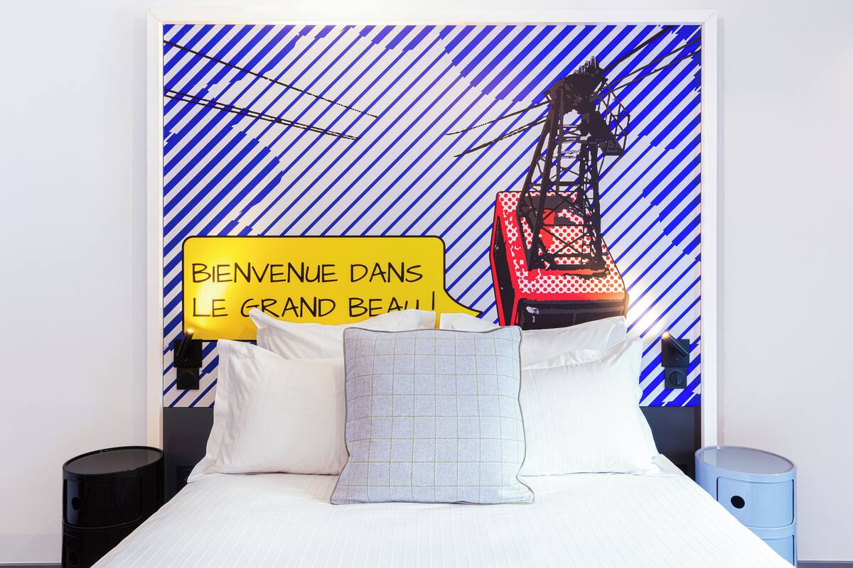 Een hotelkamer met een bed, kussens, een nachtkastje en een muur met een strepenpatroon en een bord.