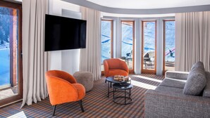 Un salon moderne doté d’un téléviseur à écran plat, de deux fauteuils orange, d’un canapé gris et d’un tapis à motifs.