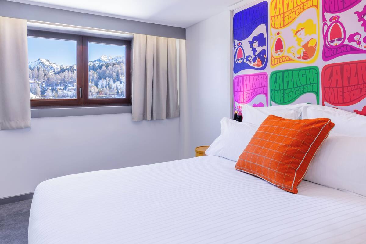 Een hotelkamer met een groot bed, een raam met gordijnen en kleurrijke decoratie aan de muur.