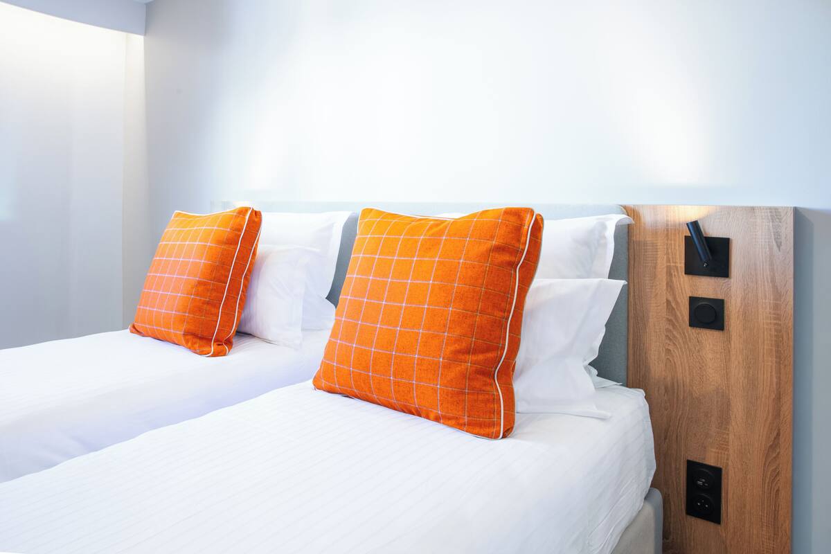 Een hotelkamer met twee bedden, elk voorzien van witte beddengoed en oranje kussens.