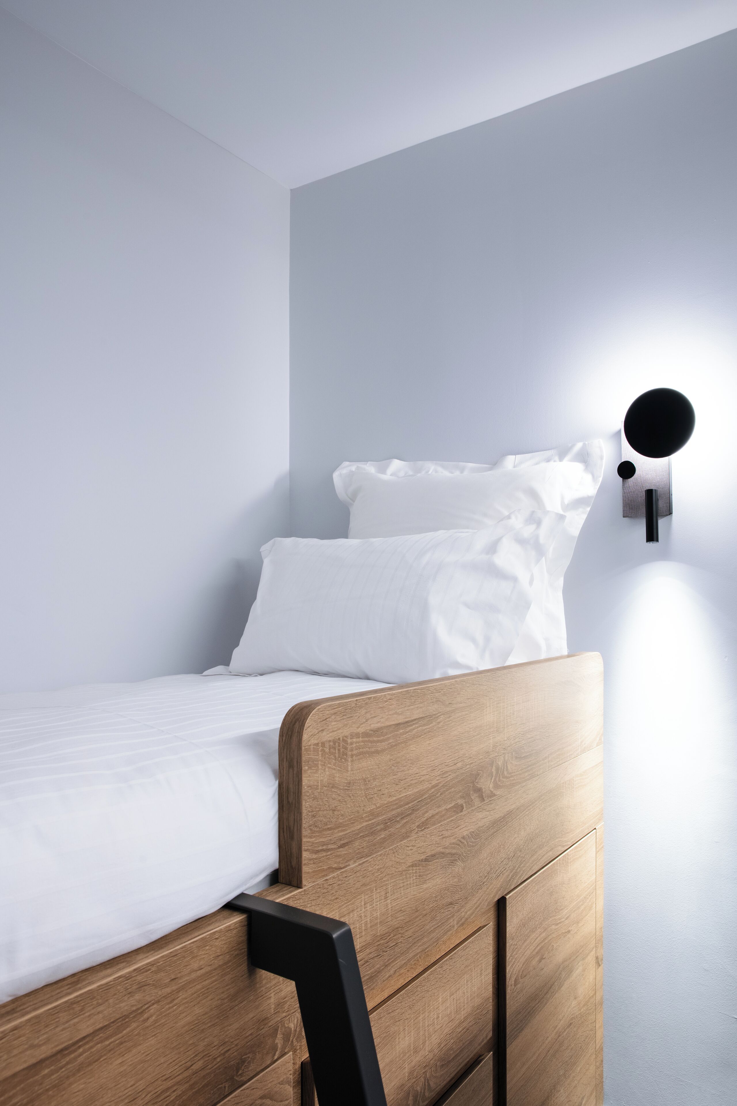 A single bed with a wooden headboard and white bedding in a room with light blue walls.